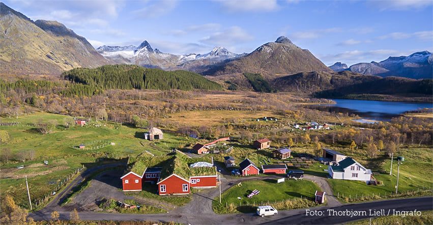 Tunet på Livland Gård sett fra luften, med røde hus, torvtak og fjellene omkring